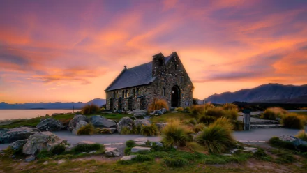 Sunset casts warm hues over the Church of St Martha-on-the-Hill, framed by rocky terrain and distant mountains in this 4K Ultra HD desktop wallpaper.