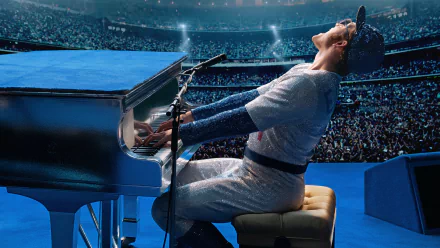 Taron Egerton as Rocketman in a stadium, passionately playing piano and singing into a microphone, captured in a vibrant 4K Ultra HD movie scene from RocketMan (2019).