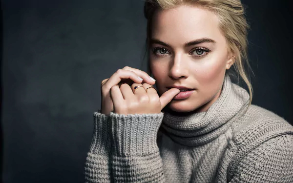HD desktop wallpaper featuring Australian actress Margot Robbie with blonde hair and blue eyes, wearing a cozy grey sweater and posing thoughtfully.