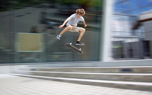 A young skateboarder performs an impressive trick mid-air in front of a modern building, capturing the dynamic energy of skateboarding and sports in this HD PC desktop wallpaper.