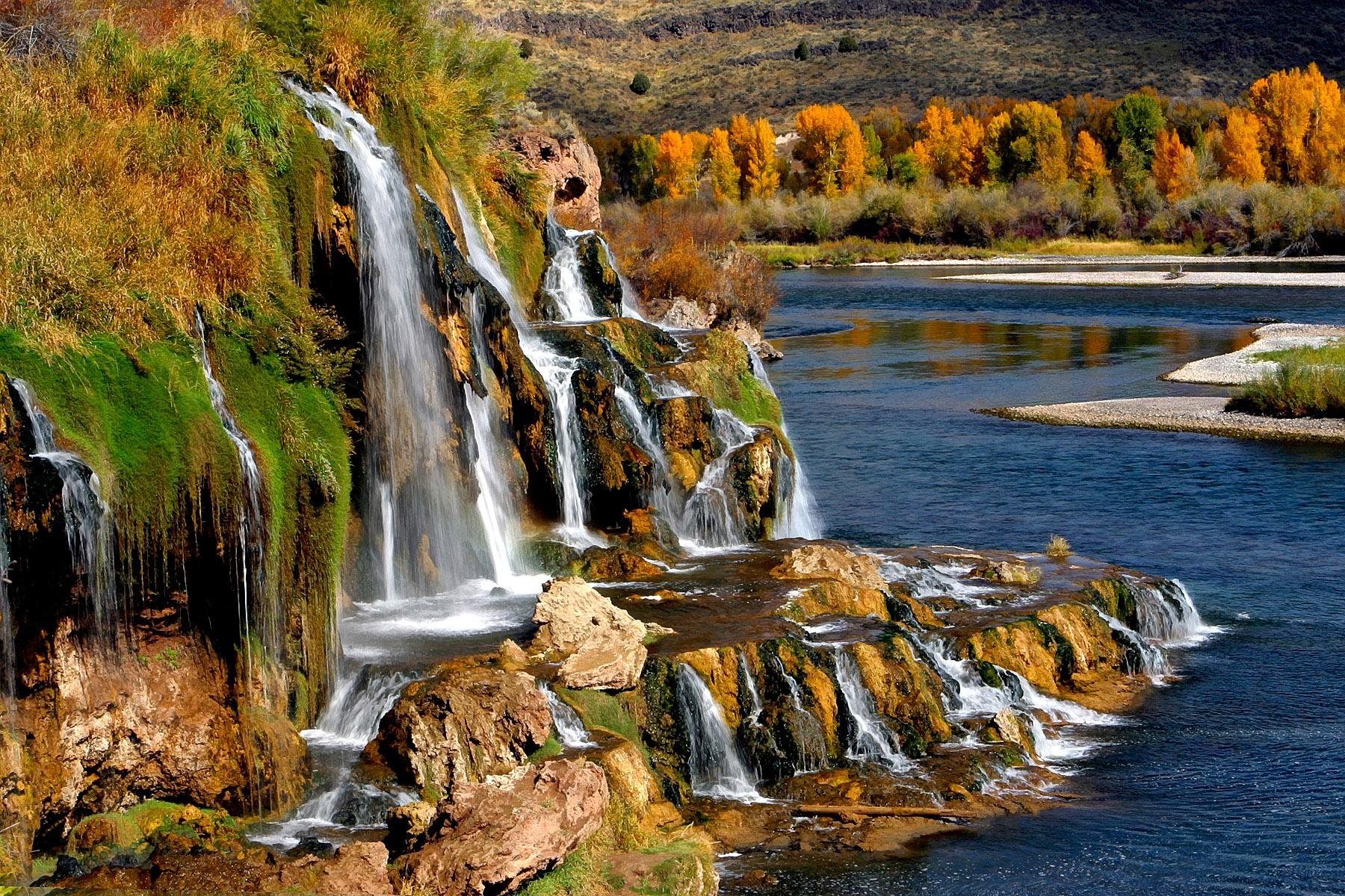 HD PC desktop wallpaper showcasing a vibrant nature scene with cascading waterfalls flowing into a river, surrounded by autumn foliage and rocky terrain.