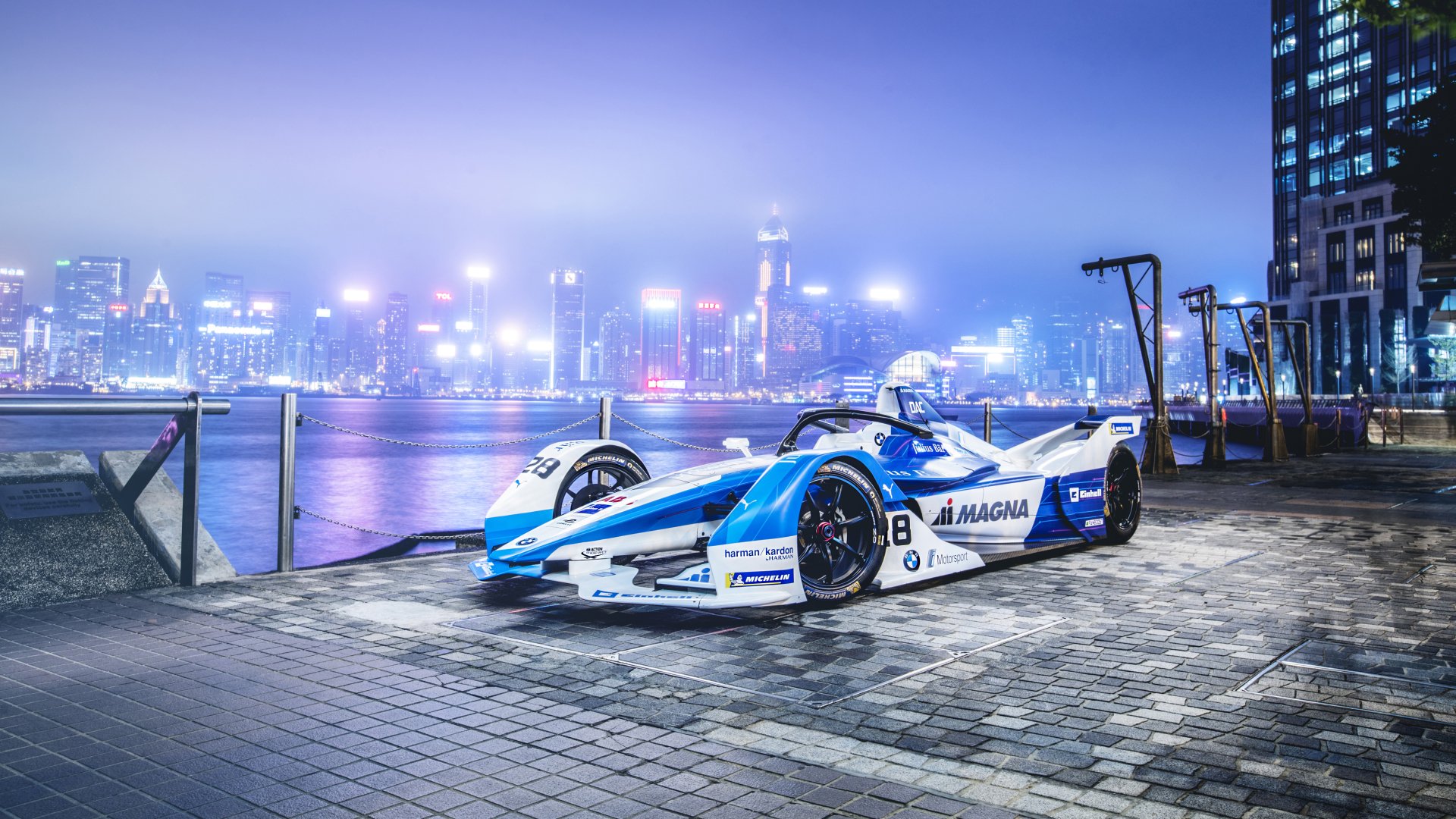 BMW iFE.18 F1-style race car parked on a waterfront promenade at night with illuminated cityscape; 4K Ultra HD PC desktop wallpaper background.