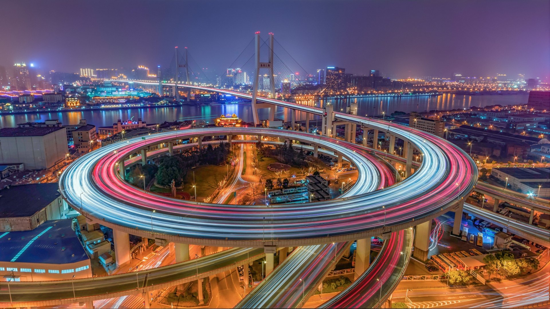 Night aerial view of Shanghai's Nanpu Bridge spiral interchange and highways with vibrant light trails in a time-lapse style — HD PC desktop wallpaper.