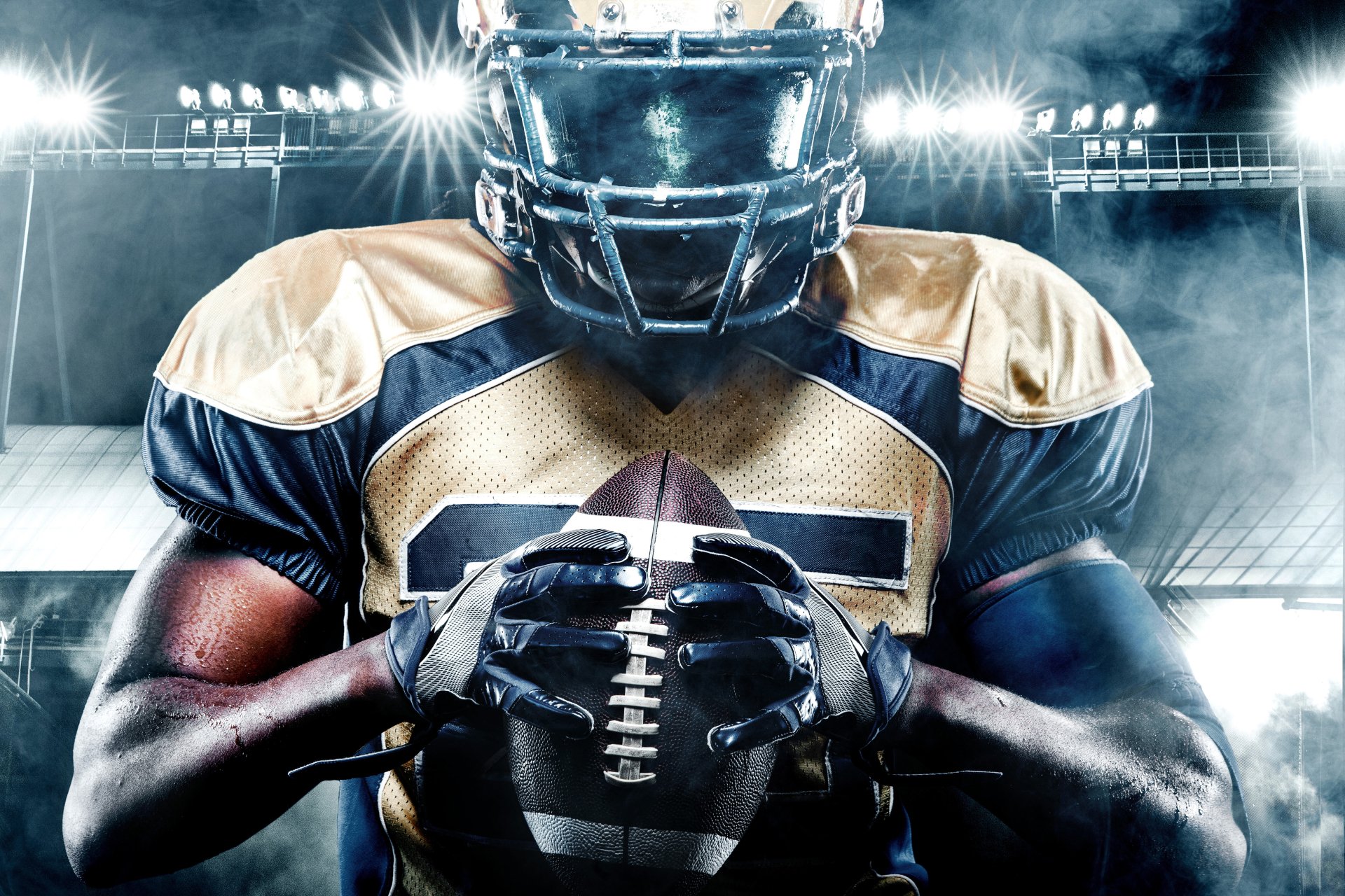 Intense close-up of a football player clutching a ball under stadium lights — Sports 5K Ultra HD PC desktop wallpaper and background.