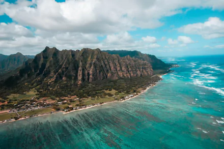 Aerial HD PC desktop wallpaper showcasing Honolulu's coastline on the island, with rugged mountains meeting clear blue ocean waters under a partly cloudy sky.