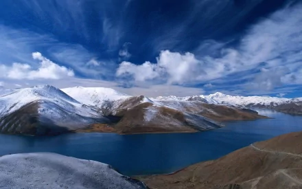 A serene landscape of a snow-capped mountain range surrounding a tranquil lake in Norway, under a vibrant blue sky with wispy clouds, showcasing the beauty of nature.