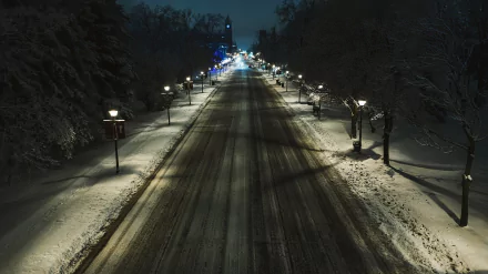 Snow-covered road at night illuminated by a row of lamp posts, framed by snow-laden trees, creating a serene winter scene for an HD PC desktop wallpaper.