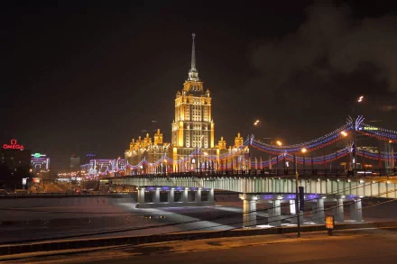 A stunning night view of a beautifully illuminated bridge in Moscow, with the ornate architecture of a nearby building adding to the vibrant cityscape, showcased in 4K Ultra HD.