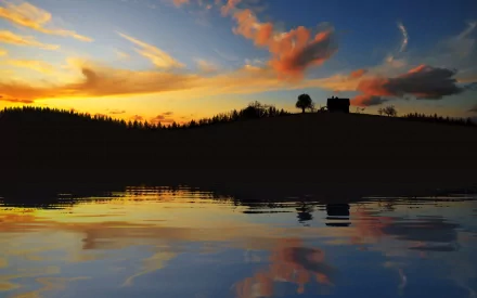 HD desktop wallpaper showing a serene sunset over a lake with clouds reflecting on the water and a house silhouetted against the natural landscape.