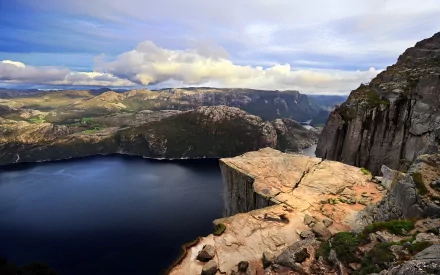 A breathtaking view of Preikestolen in Norway, featuring a dramatic cliff overlooking a serene fjord, framed by blue skies and scattered clouds, showcasing stunning natural beauty.