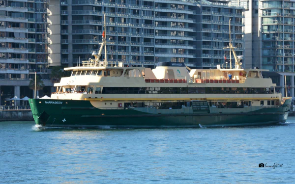 2K Quad HD PC desktop wallpaper showing a green-and-cream ferry boat (vehicle) cruising on blue water past glass high-rise waterfront buildings.