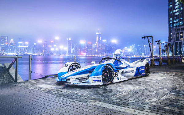 BMW iFE.18 F1-style race car parked on a waterfront promenade at night with illuminated cityscape; 4K Ultra HD PC desktop wallpaper background.
