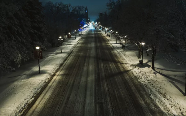 Snow-covered road at night illuminated by a row of lamp posts, framed by snow-laden trees, creating a serene winter scene for an HD PC desktop wallpaper.