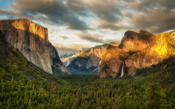 A stunning 4K Ultra HD desktop wallpaper showcasing Yosemite National Park’s iconic granite cliffs and lush forest under a dynamic sky at sunset.