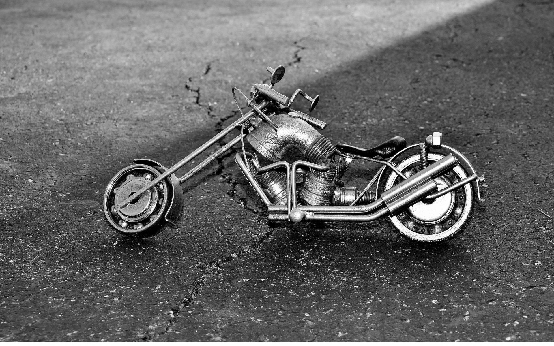 Black and white HD desktop wallpaper featuring a detailed metal toy motorcycle on a textured surface, showcasing man-made craftsmanship.