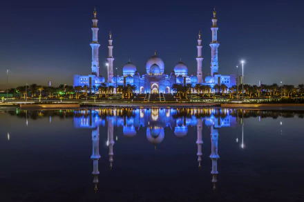 Nighttime view of a beautifully illuminated mosque in the United Arab Emirates, with its detailed architecture and reflection shining on calm water.