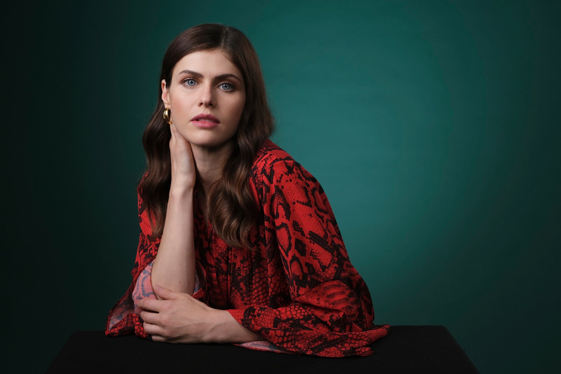 HD desktop wallpaper featuring American actress Alexandra Daddario with blue eyes, brunette hair, and red lipstick, wearing a red patterned top against a green background.