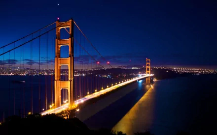 A stunning view of the Golden Gate Bridge illuminated at night, reflecting beautifully in the bay, showcasing the vibrant city lights of San Francisco.