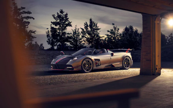 8K Ultra HD PC desktop wallpaper of a silver Pagani Huayra supercar parked at dusk, a low-slung vehicle framed by a garage opening with silhouetted trees in the background.