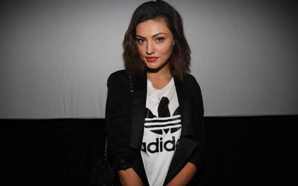 Brunette woman in a black jacket over a white Adidas tee, seated against a gray-to-black backdrop, framed as an HD PC desktop wallpaper.