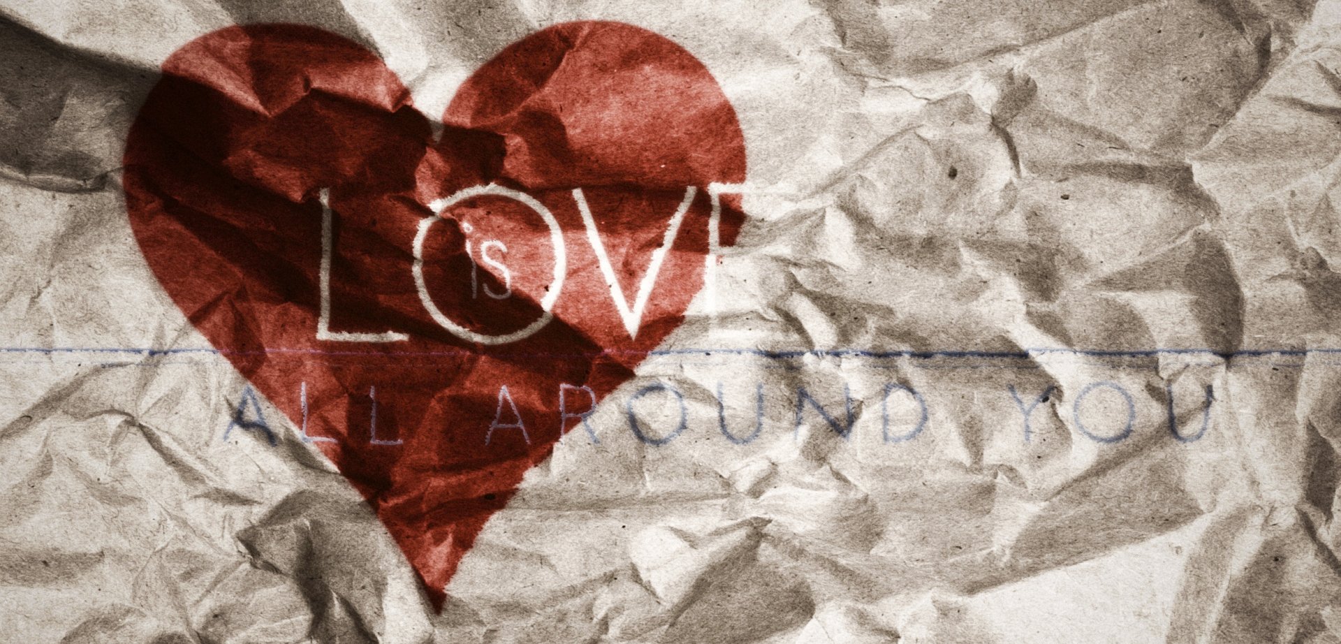 Artistic HD wallpaper featuring a crumpled background with the words Love is all around you inside a red heart, conveying a message of warmth and affection.