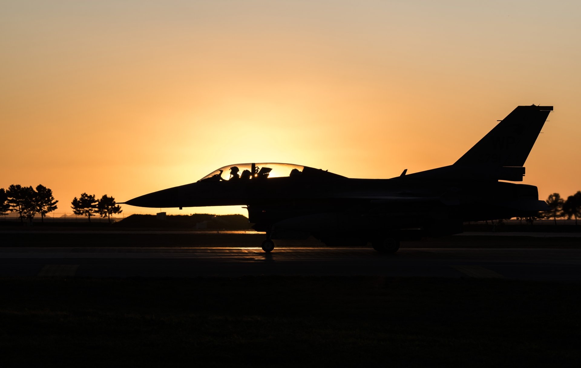 Silhouette of a General Dynamics F-16 Fighting Falcon jet fighter on the runway at sunset, captured in 4K Ultra HD for a striking military aircraft wallpaper.