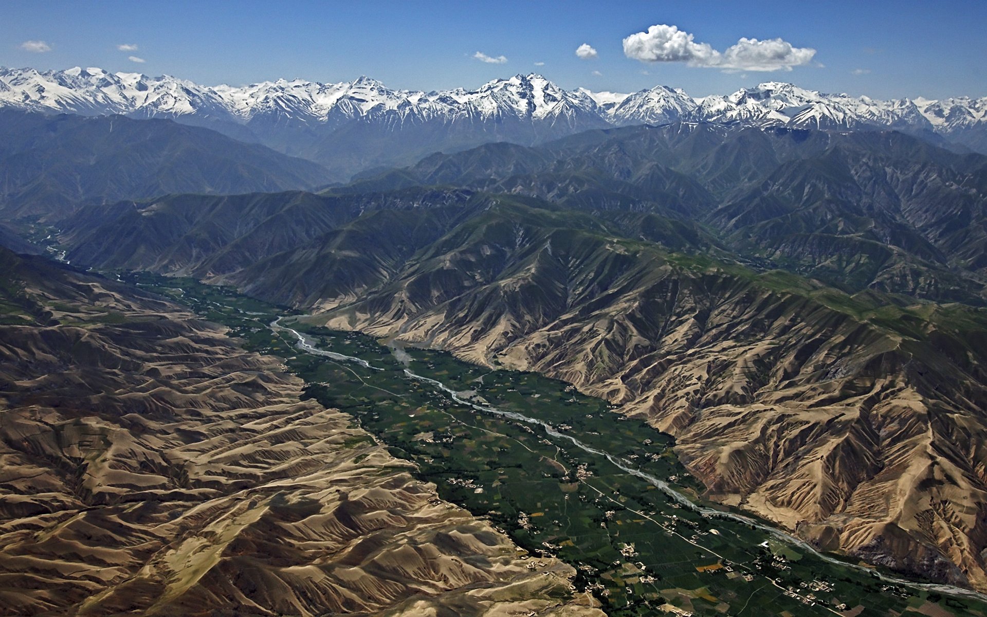 Aerial view of New Zealand's Hooker Valley featuring a winding river, snow-capped mountains, alluvial terrain, and a bright blue sky with scattered clouds.