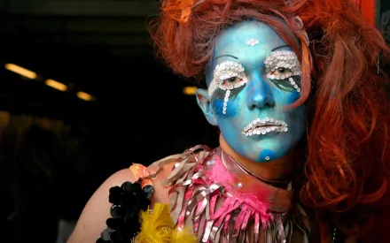 A woman with vibrant red hair and intricate white and blue makeup, wearing a colorful, textured costume, featured as an HD PC desktop wallpaper and background.