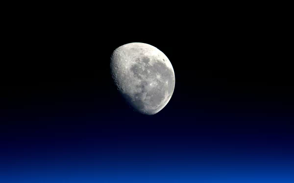 HD desktop wallpaper featuring a clear image of the moon against a gradient blue to black sky, capturing the natural beauty of the lunar surface.