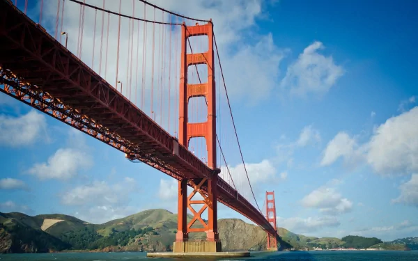 2K Quad HD desktop wallpaper: Golden Gate Bridge spanning a blue sky with clouds and a faint rainbow over the bay, red man-made suspension bridge shot from a low angle.