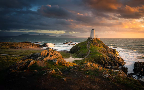 A man-made lighthouse stands on a rocky path along the Welsh coast, overlooking the sea and horizon under a dramatic, colorful sky.