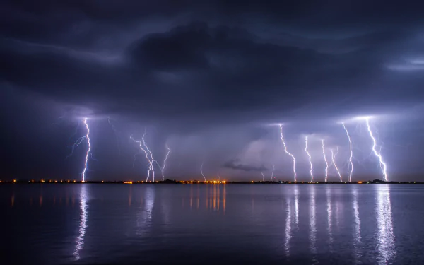 4K Ultra HD photography of multiple lightning bolts striking over a calm body of water beneath a stormy night sky, captured as a dramatic desktop wallpaper.