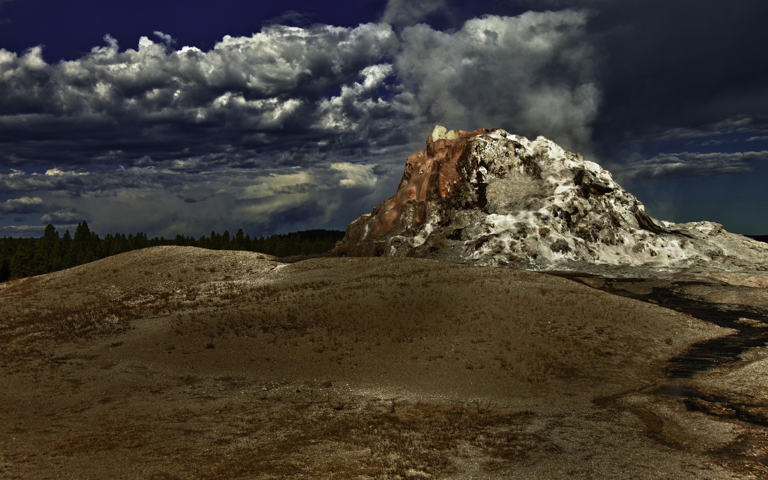 White Dome Geyser erupting amidst a Yellowstone forest with dramatic clouds (HDR wallpaper).