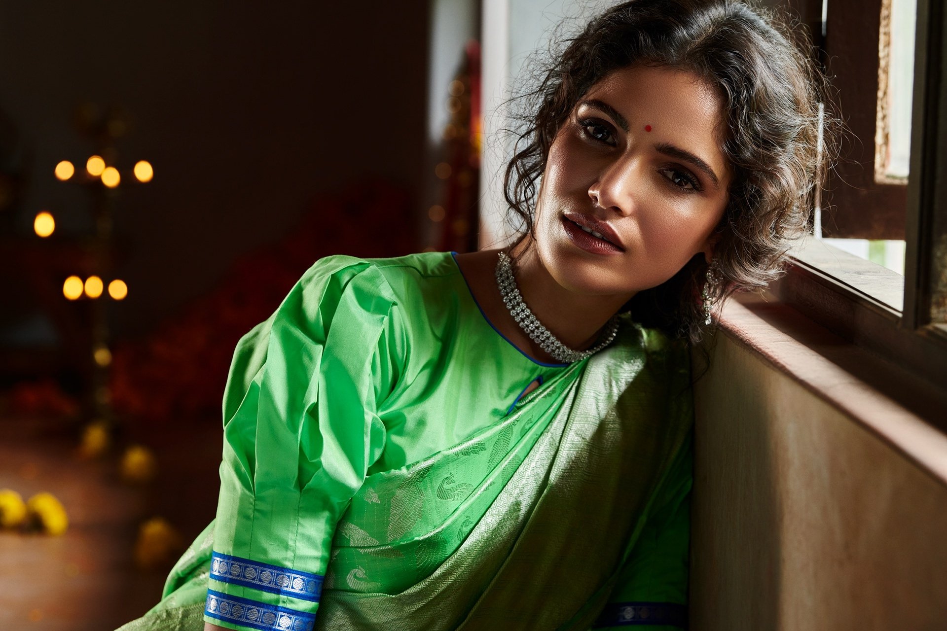 Brunette Indian model Vartika Singh poses in a vibrant green saree by a window, captured in an HD desktop wallpaper showcasing traditional elegance.