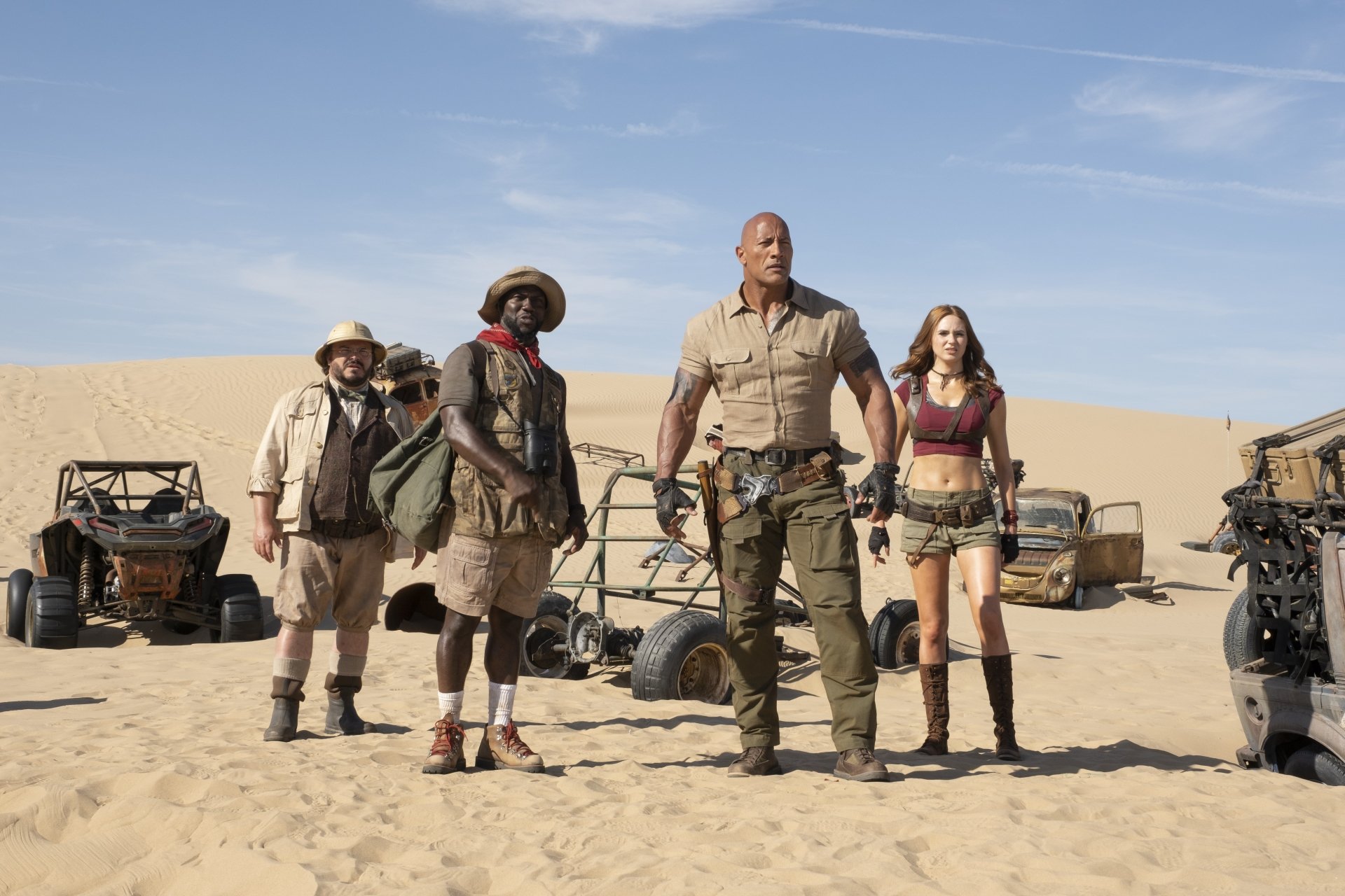 5K Ultra HD PC desktop wallpaper: four actors from Jumanji: The Next Level in desert adventure gear stand by dune buggies under a bright blue sky.