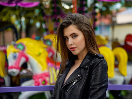 Brunette woman model in a black leather jacket and lipstick, shallow depth of field with colorful carousel behind — 2K Quad HD PC desktop wallpaper/background.