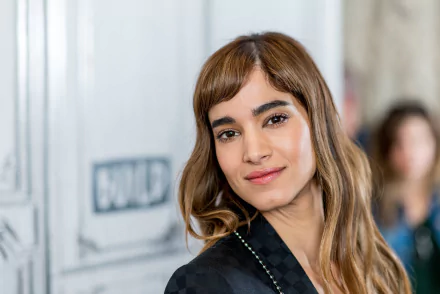 Close-up HD portrait of brunette French actress Sofia Boutella with brown eyes, softly smiling against a blurred background.