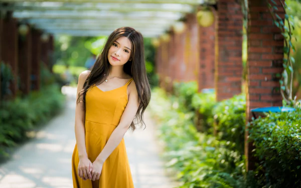 4K Ultra HD desktop wallpaper: brunette woman model with long hair in a yellow dress, shallow depth of field on a sunlit garden path.