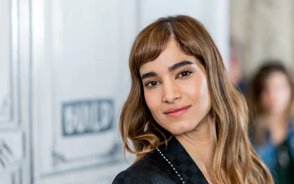 Close-up HD portrait of brunette French actress Sofia Boutella with brown eyes, softly smiling against a blurred background.