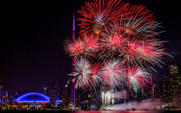 5K Ultra HD PC wallpaper photo of Toronto, Canada at night: CN Tower and city lights lit by vibrant fireworks over the waterfront.