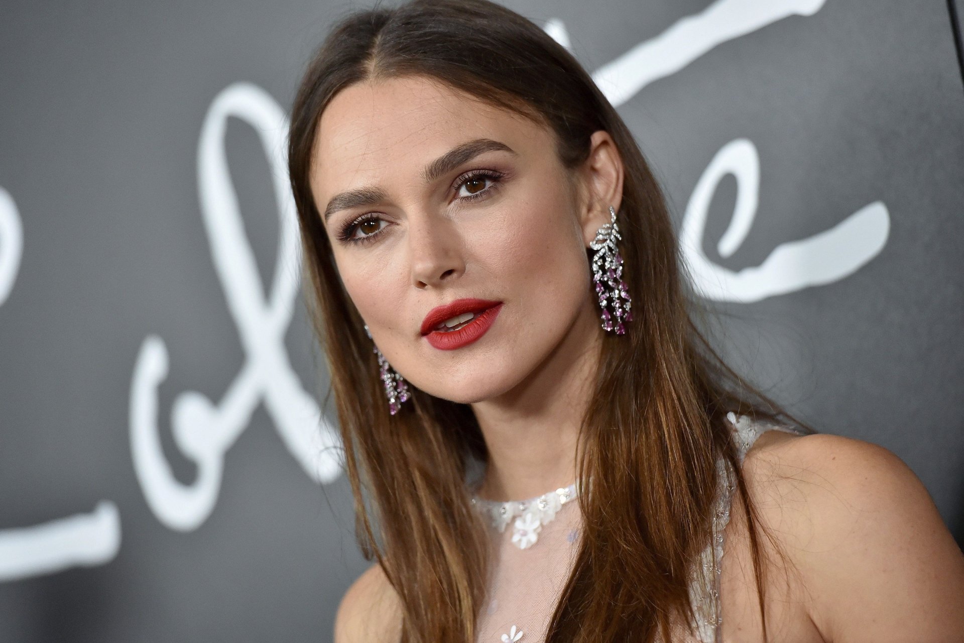 Close-up portrait of a brunette woman's face with brown eyes, red lipstick and sparkling statement earrings, elegant 2K Quad HD desktop wallpaper.