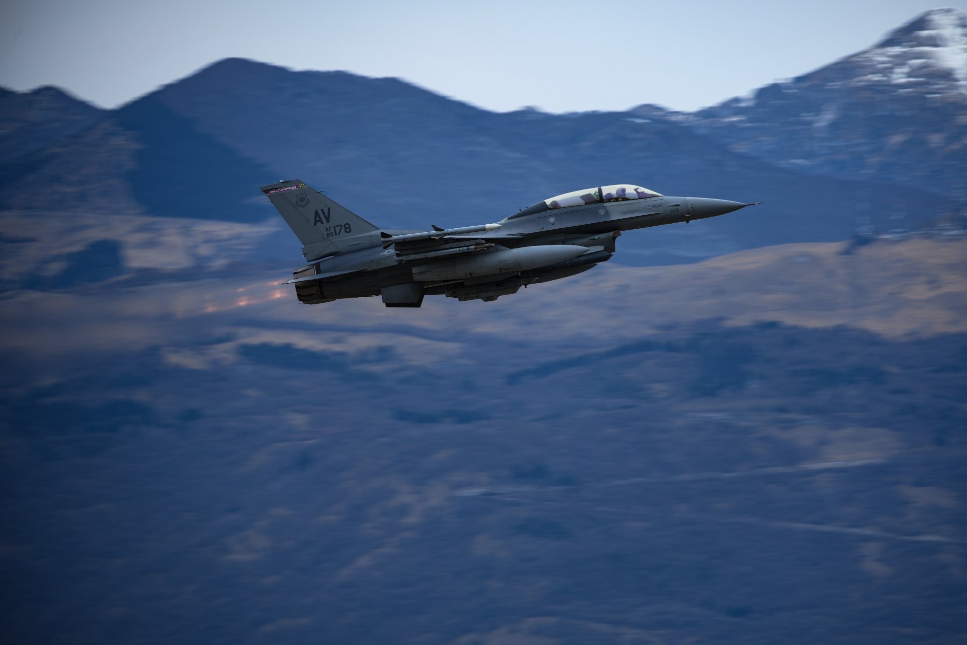 A General Dynamics F-16 Fighting Falcon warplane jet fighter flies over mountainous terrain, captured in stunning 8K Ultra HD detail for a PC desktop background.