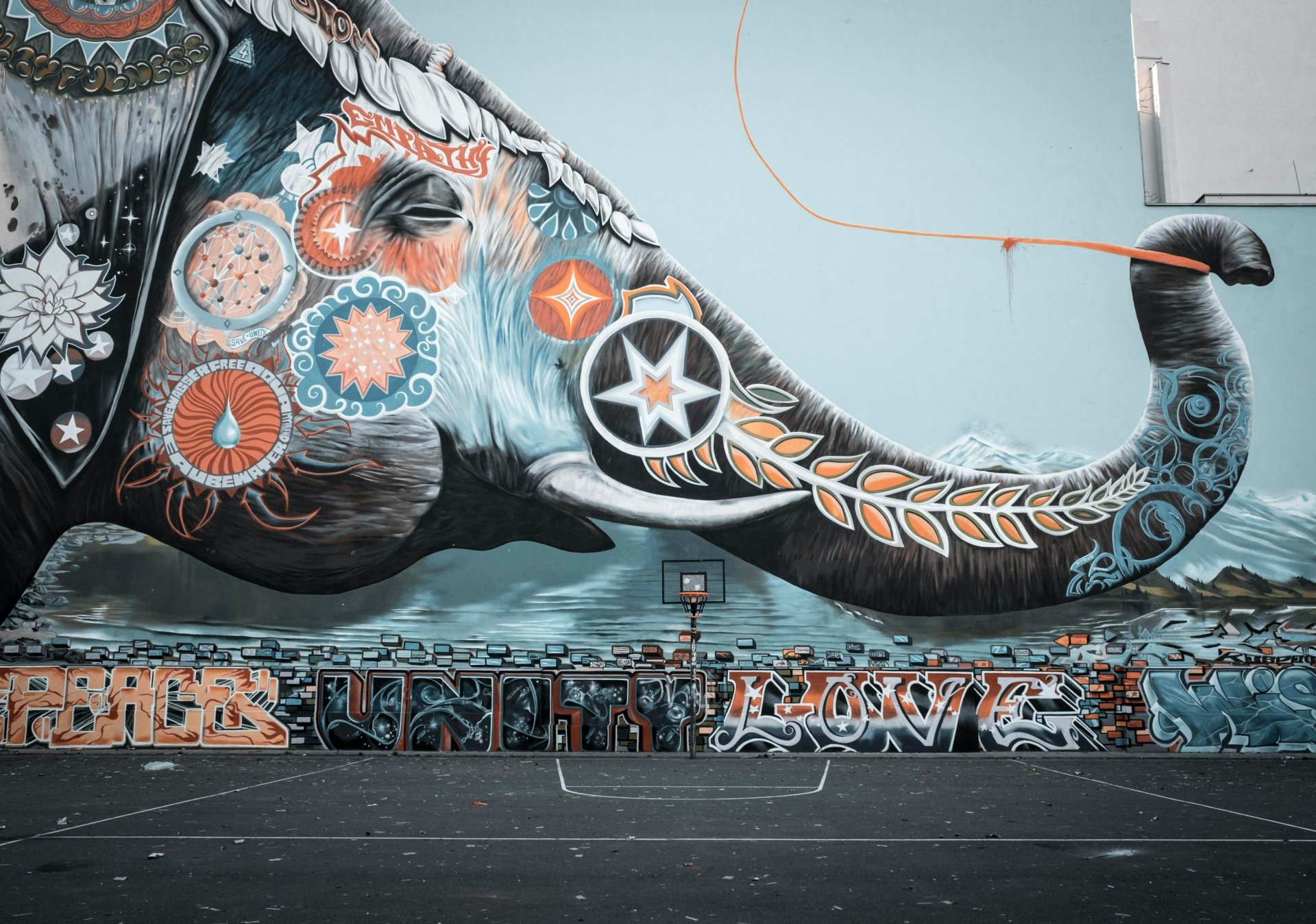 Artistic graffiti elephant mural across a city wall and empty court, vibrant floral, star and geometric motifs — 4K Ultra HD PC Desktop Wallpaper and Background.