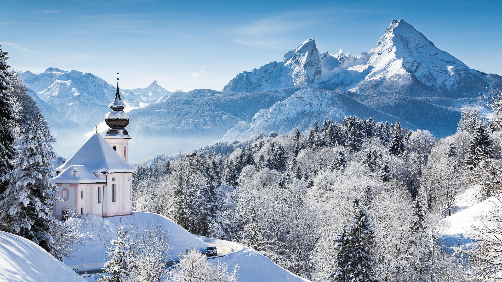 A serene 4K Ultra HD winter scene featuring a snow-covered church nestled among frosted trees with majestic mountains in the background.