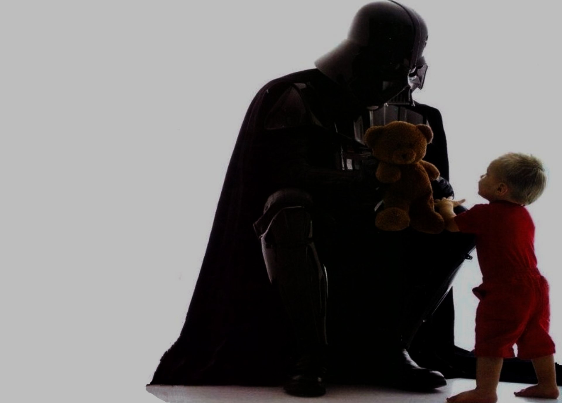 A silhouette of Darth Vader from Star Wars kneeling beside a child holding a teddy bear, creating a striking Sci-Fi scene for an HD desktop wallpaper.