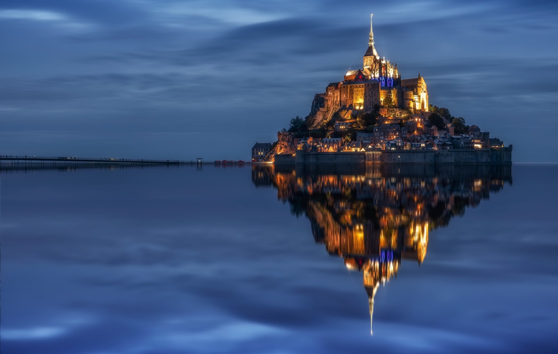 Mont Saint-Michel monastery illuminated at night, reflecting perfectly on the calm water in France, captured as an HD desktop wallpaper and background.