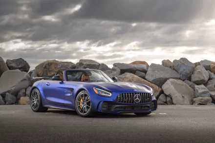 A blue Mercedes-AMG GT R Roadster supercar parked by large rocks under a cloudy sky, presented in 4K Ultra HD as a high-quality desktop wallpaper.