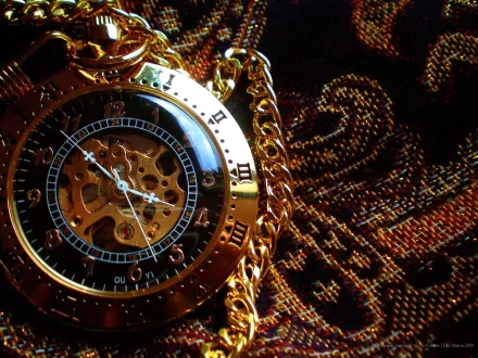 HD desktop wallpaper featuring a close-up of an intricate golden steampunk pocket watch with a visible gear mechanism, set against a richly patterned fabric background. Sci-fi and steampunk elements.