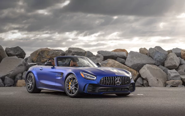 A blue Mercedes-AMG GT R Roadster supercar parked by large rocks under a cloudy sky, presented in 4K Ultra HD as a high-quality desktop wallpaper.
