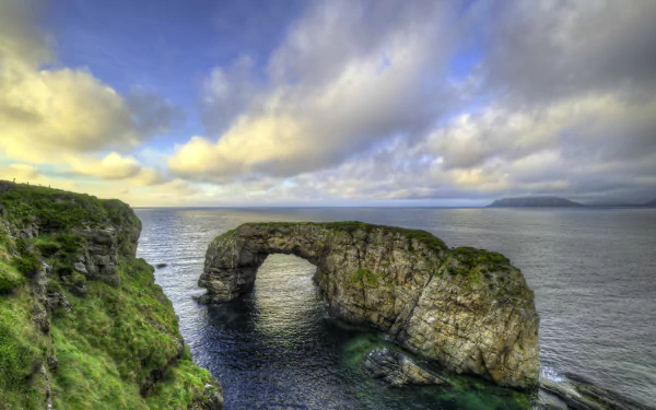 4K Ultra HD wallpaper of Ireland’s natural stone arch rising from the ocean, framed by a dramatic horizon and cloudy sky, showcasing stunning coastal scenery.